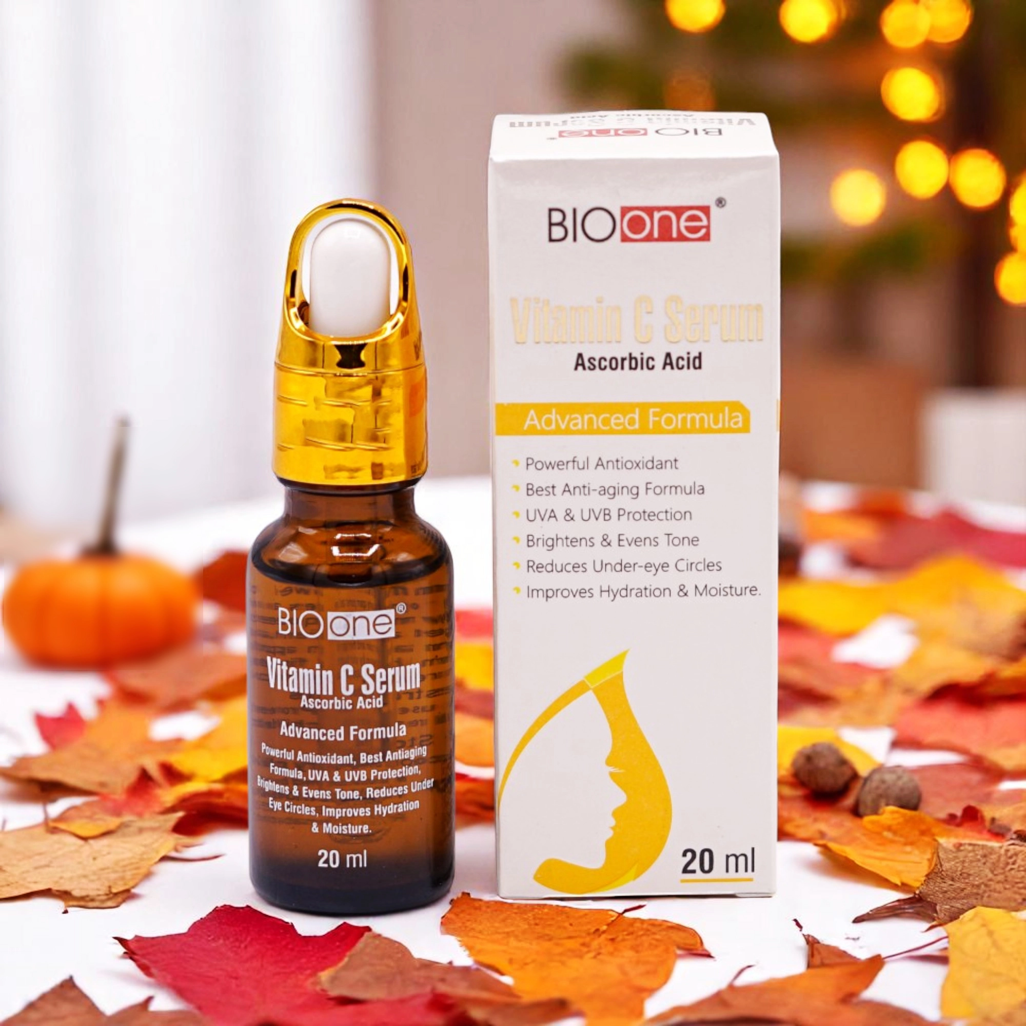 Bio One Vitamin C Serum with Ascorbic Acid, 20ml amber dropper bottle with a gold top and a white and black label, alongside its white and gold box, set against an autumn-themed background with colorful leaves and a small pumpkin.